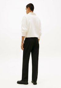 Weißer Pullover mit Kragen, kombiniert mit schwarzen Hosen. Das Outfit hat eine lässige Passform und einfarbige Farben. Schwarze Schuhe vervollständigen den Look.