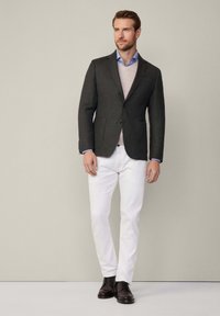 Blazer grigio in lana sovrapposto a un maglione beige, abbinato a una camicia azzurra e pantaloni bianchi, completato da scarpe stringate marroni scure.