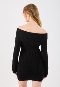 Vestido negro sin mangas hecho de tela acanalada, con mangas largas, diseño ajustado y una superficie texturizada.
