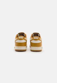 Nike sneakers med gult læder og hvide accenter. Lavt design, polstret krave og tekstureret gummisål med synligt dækmønster.