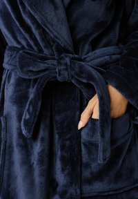 Bata de baño de felpa suave en azul marino, con cintura atada, amplio cuello y dos bolsillos frontales. La tela tiene una apariencia de felpa texturizada.