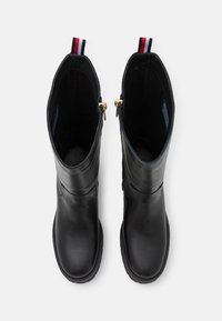 Bottines en cuir noir avec une finition lisse, tige haute, détail de fermeture éclair doré et une languette de tirage rayée rouge et marine en haut.