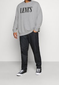 Sudadera gris con el logo negro de "LEVI'S", combinada con jeans oscuros de mezclilla y zapatillas negras con suelas blancas. Corte relajado, textura suave.