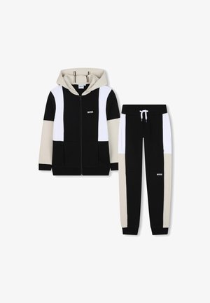 Ensemble de survêtement à capuche en noir, beige et blanc. La veste zippée présente un contraste de couleurs et des poches. Le pantalon dispose d'une taille élastique et de poignets élastiques.