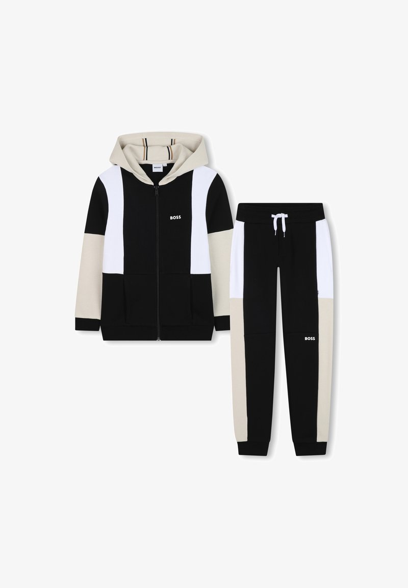 Conjunto de fato de treino com capuz em preto, bege e branco. A jaqueta com fecho éclair apresenta blocos de cor e bolsos. As calças têm cintura elástica e punhos.