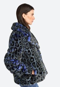Veste en fausse fourrure avec un design léopard noir et bleu, col oversize, poches latérales et texture douce.