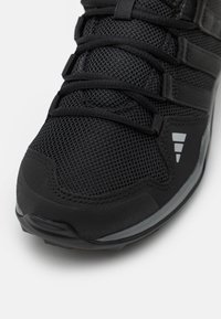 Czarne buty sportowe z siateczkową cholewką, teksturowanym wykończeniem, wzmocnionym noskiem oraz kontrastującymi szarymi akcentami na podeszwie i boku.