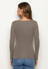 Camicia a maniche lunghe aderente di colore taupe, con colletto a girocollo e texture morbida, abbinata a jeans in denim a vita alta.