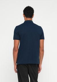 Camisa polo azul-marinho com mangas curtas, tecido texturizado e um colarinho clássico. Sem marcas ou padrões visíveis na parte de trás.