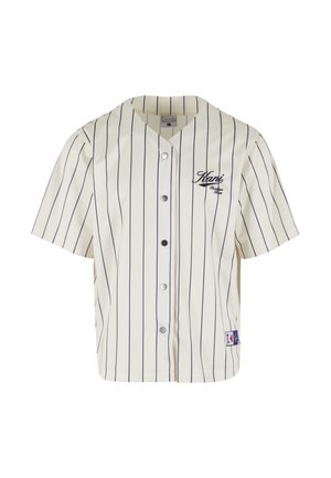 Krekliņš ar pogām beisbola stilā krēmkrāsā ar tumsā zilām vertikālām strīpām. Īsās piedurknes, apaļš apkaklis un izšūta logo uz krūtīm.