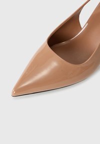 Escarpin verni beige brillant à bout pointu, présenté de face sur un fond blanc.