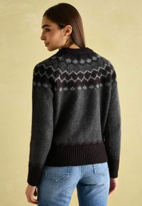 Grau gemusterter Pullover mit gestricktem Design, ausgestattet mit einem schwarzen Rippenbund und Rippenärmeln. Das Model trägt blaue Jeans und zeigt eine Rückansicht.