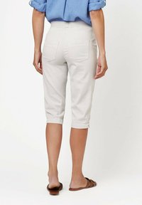 Helle beigefarbene Capri-Hosen aus Baumwolle, mit einem elastischen Bund, zwei Gesäßtaschen und umgeschlagenen Säumen, kombiniert mit braunen Sandalen.