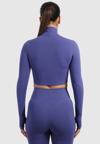 Lilla langærmet cropped sportstrøje med høj krave, glat tekstur og tætsiddende design, parret med matchende højtaljede leggings.