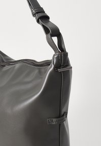 Sac à main en cuir gris avec une texture lisse, une fermeture éclair et une bandoulière avec un design noué et un accent en métal.
