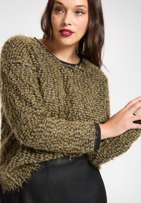 Sweter o luźnym kroju w oliwkowej zieleni z teksturowanym splotem, czarnymi mankietami oraz metalicznymi nitkami, z okrągłym dekoltem.