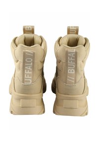 Zapatillas altas beige con tejido texturizado, acolchado reforzado y acentos de logo vertical en la parte trasera. Presentan una suela resistente y tiradores.