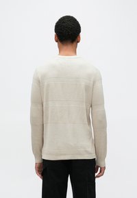 Beige genser med lange ermer og teksturerte horisontale striper. Strikket stoff, rund halsutskjæring og ribbestrikkede mansjetter og nederkant. Minimalistisk design.