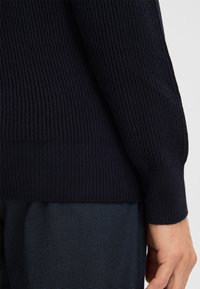 Marineblauer, gerippter Pullover mit strukturiertem Strick, passenden Manschetten und einem Taillenbund, kombiniert mit dunkelblauen, strukturierten Hosen.