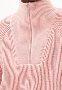 Pull-over rose clair avec un col montant et une fermeture éclair, présentant une texture côtelée et des motifs de tricot détaillés sur les épaules.