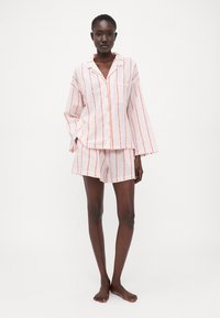Lättvikts pyjamasset i bomull med rosa och orange vertikala ränder, en skjorta med krage och knappar, samt matchande shorts med elastiskt midjeband.