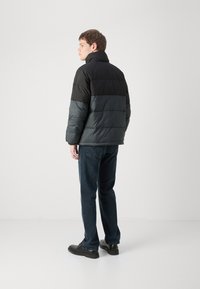Giacca imbottita nera e grigia, con colletto alto, tessuto testurizzato e design trapuntato. Indossata con jeans blu sbiaditi e scarpe nere.