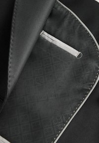 Schwarzes Stoffinterieur mit einer strukturierten grauen Fütterung, die ein sich wiederholendes quadratisches Muster zeigt; enthält eine kleine Tasche mit einem Band.