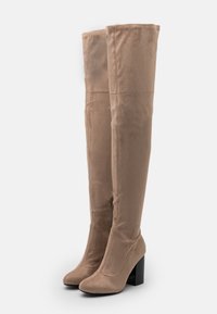 Beige Wildlederstiefel in Knöchelhöhe mit einem quadratischen schwarzen Absatz, glatter Textur und einer taillierten Passform. Verstärkte Nähte entlang der Nähte sichtbar.