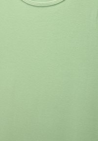 Jednorodna, jasna zielona tkanina o teksturze, z delikatnym cieniem i zagięciami z tyłu.