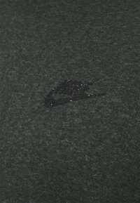 Mörkgrön Nike t-shirt gjord av mjukt, texturerat tyg; har en svart logotyp med färgglada prickar på bröstområdet.