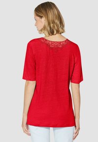 Rode t-shirt met korte mouwen en een geschulpte kantdetail langs de achterkant van de halslijn. Gemaakt van textuurstof, casual pasvorm.