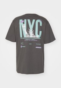 Pilka medvilninė marškinėliai su ryškiu „NYC“ tekstu, Statulos laisvės grafika ir daugiakomponentės akcentai. Galima skalbti mašinoje.