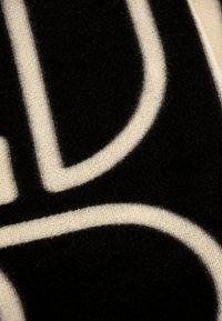 Primo piano di un tessuto nero con linee geometriche bianche che formano forme arrotondate e rette, mostrando dettagli della trama e della tessitura.