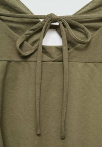 Olivově zelený bavlněný top s kapucí a šňůrkovým zavíráním. Texturovaná látka s viditelnými švy, volný střih a výřez na zadní straně.