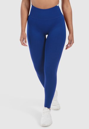 Hochtaillierte blaue Leggings aus dehnbarem Stoff, mit einer glatten Textur und einem einfachen Design, kombiniert mit weißen Sportschuhen.