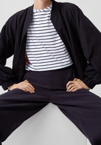 Chaqueta bomber negra, camiseta de rayas blancas y pantalones oscuros. Materiales suaves con un ajuste relajado. Incluye cierre con cremallera y puños acanalados.