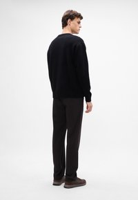 Suéter negro de punto con corte holgado, escote redondo y puños acanalados, combinado con pantalones oscuros y zapatillas marrones.