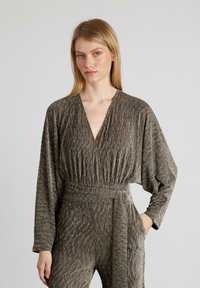 Mono gris con textura, escote en V profundo, mangas largas y cintura ajustada con un cinturón a juego. Patrón sutil de rayas verticales.