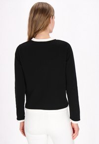 Un top negru cu manșete lungi, cu borduri albe la guler și la manșete, având un design simplu și o textură fină a materialului.