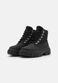 Bottines noires en suède avec un col rembourré, dotées de lacets ronds, d'œillets en métal et d'une semelle épaisse et striée.