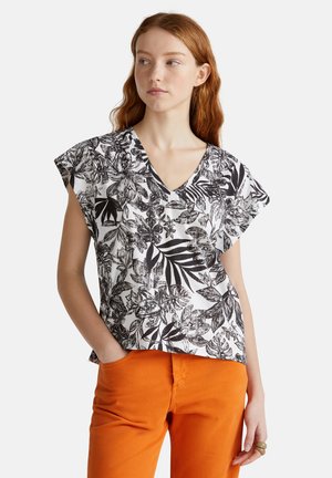 Kurzarmbluse mit V-Ausschnitt, ausgestattet mit einem schwarz-weißen Blumenmuster, kombiniert mit orangen Hosen. Leichtes Material, lässiges Design.