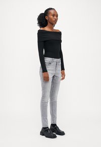Fekete bordázott off-shoulder felső, világosszürke skinny farmerrel és fekete platform cipővel párosítva. Egyszerű, testhezálló dizájn minimális díszítéssel.