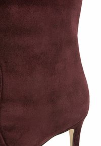Burgundowa zamszowa botka za kostkę z ostrym noskiem i wysokim obcasem, charakteryzująca się gładką teksturą i eleganckim designem bez widocznych elementów metalowych.
