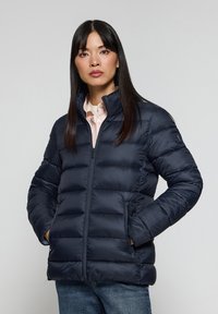 Giubbotto puffer blu navy con colletto alto, chiusura con zip e design trapuntato. Dotato di tasche laterali e realizzato in un materiale lucido e leggero.