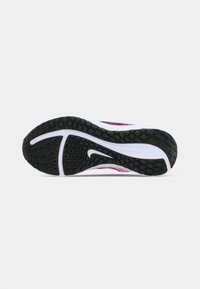 Semelle d'une chaussure de sport rose et blanche avec une semelle noire et un logo Nike swoosh blanc sur un fond clair.