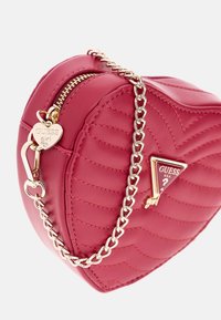 Hartvormige rode handtas van doorgestikt kunstleer, met een gouden kettingriem en een hanger met een hartdetail en het merklogo.