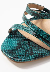 Turska ja mustad maokese sandaalid on varustatud risttavate rihmade, ruudukujulise varbaga ja pruuni sisetalla ning õmblustega detailidega.