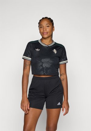 T-shirt noir court avec un motif floral, des rayures vertes sur les épaules et un logo brodé. Associé à un short noir, affichant un détail de logo.