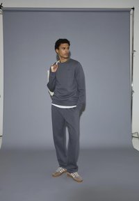 Grå sweatshirt och byxor av mjukt material, med rundad halsringning, avslappnad passform och subtil branding. Skorna är gråa i mocka med vita ränder.