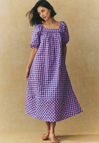 Maxikleid im pink-blauen Karomuster, viereckiger Ausschnitt, puffige Ärmel und fließende Silhouette. Getragen mit flachen braunen Schuhen.